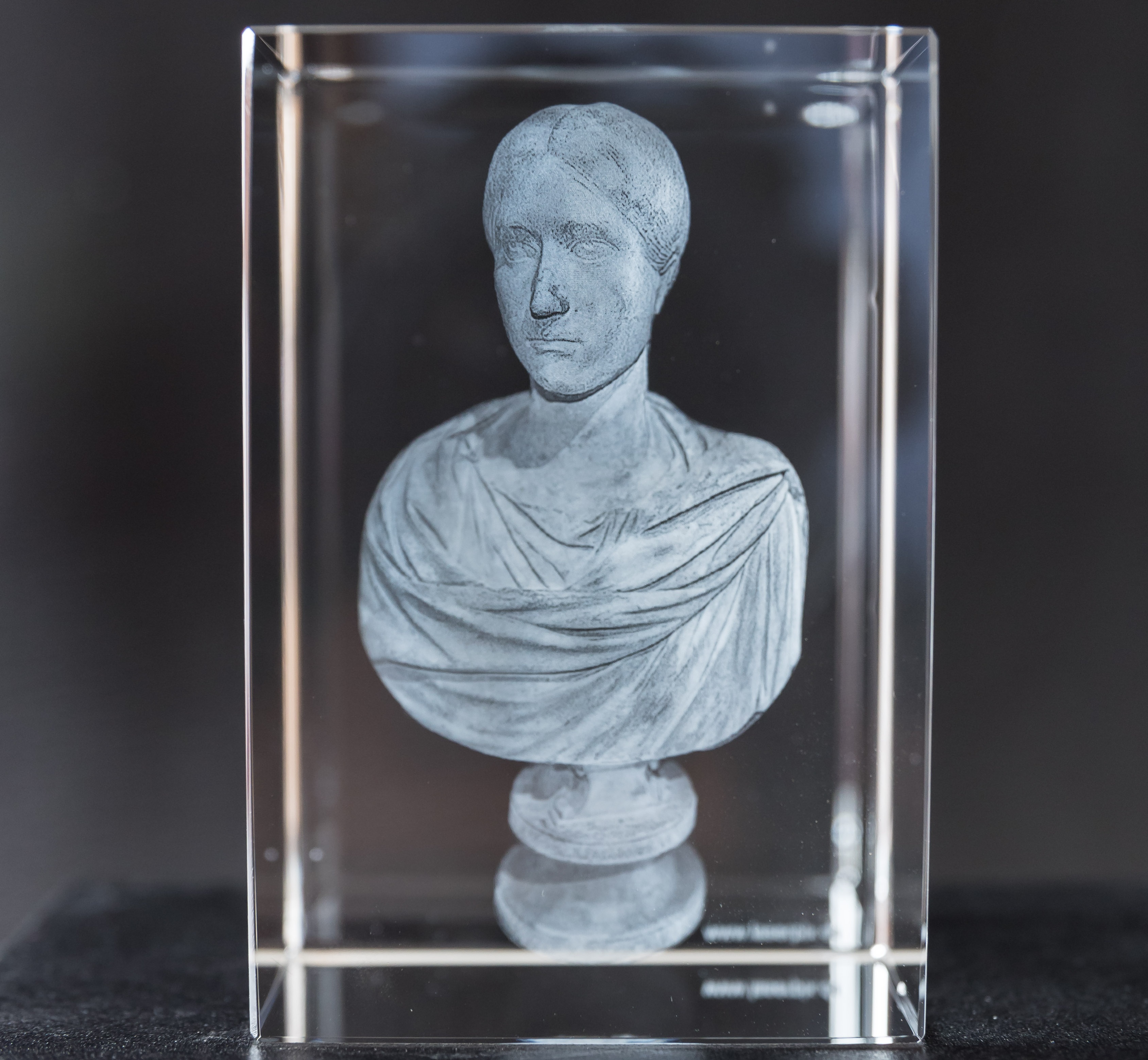 Ein hochkant stehhender Glaswürfel mit der 3D-Gravur einer Damen-Büste mit römischer Bekleidung und römischer Frisur
