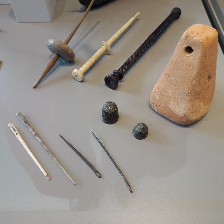 Römische Werkzeuge zur Textilherstellung: Nähnadeln und Spindeln aus Bein und Metall, zwei metallene Fingerhüte, ein tönernes Webgewicht