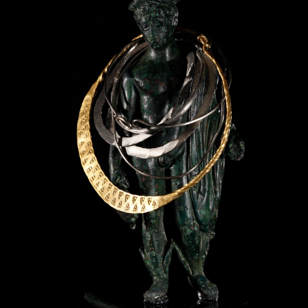 Römische Bronzestatuette des Gottes Merkur mit Reisemantel, Botenstab, Flügelstiefeln und Geldbeutel. Um ihren Hals liegen wie bei der Auffindung silberne Ohr- und Schläfenringe, ein Goldring und zu ihren Füßen bronzene Orakelstäbchen. LWL-Museum für Archäologie Herne