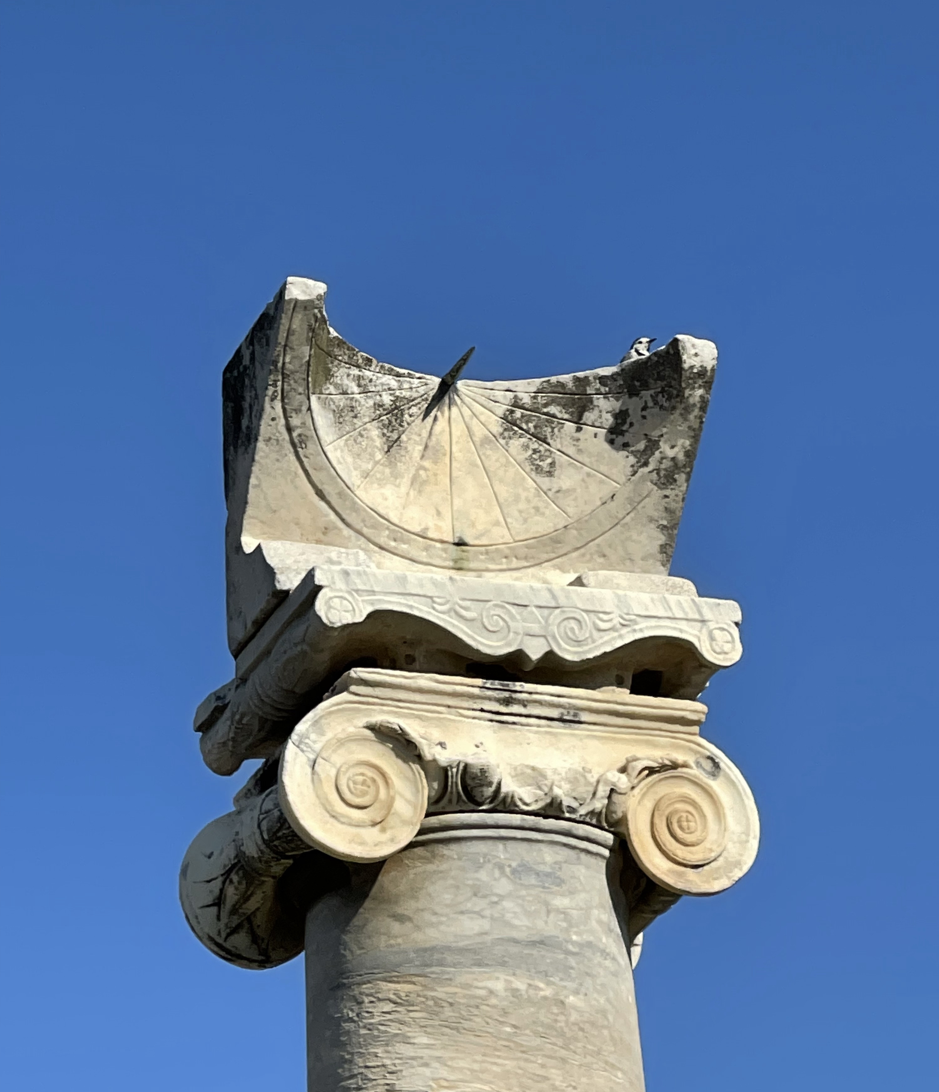 Aufnahme einer steinernen Sonnenuhr auf einer Steinsäule vor blauem Himmel